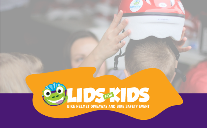 Volunteer placing a bicycle helmet on a child during the Lids for Kids bike helmet giveaway and bike safety event.